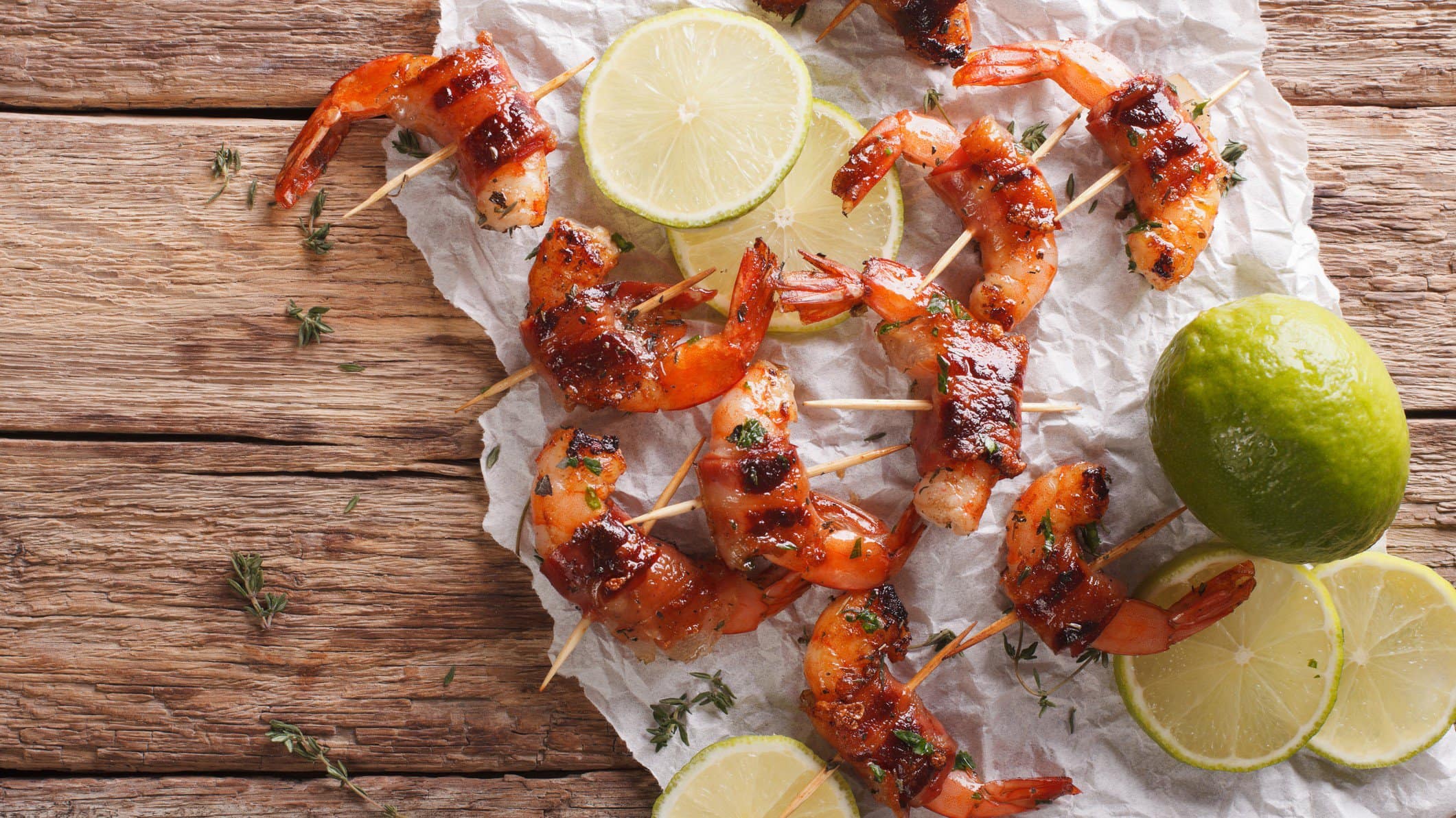 Shrimps im Speckmantel auf einem Küchenpapier. Daneben eine aufgeschnittene Limette.