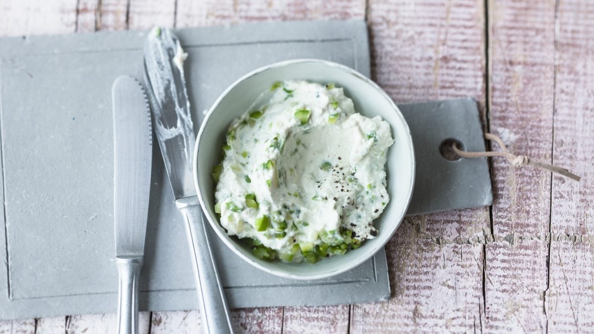Spargel-Ricotta-Creme in einer weißen Schale auf einem Schneidebrett. Daneben zwei Messer. Das Ganze auf einem hölzernen Untergrund.
