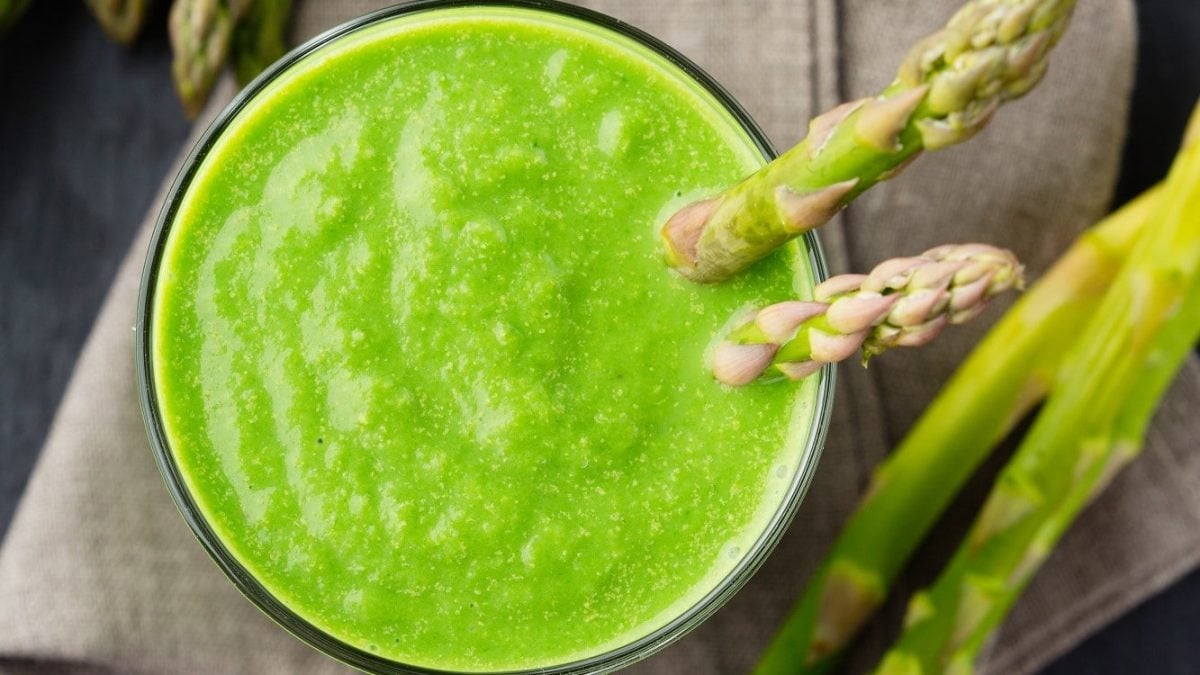Grüner Spargel-Smoothie in einem Glas, garniert mit zwei grünen Spargel-Stangen auf einem hölzernen Tisch.