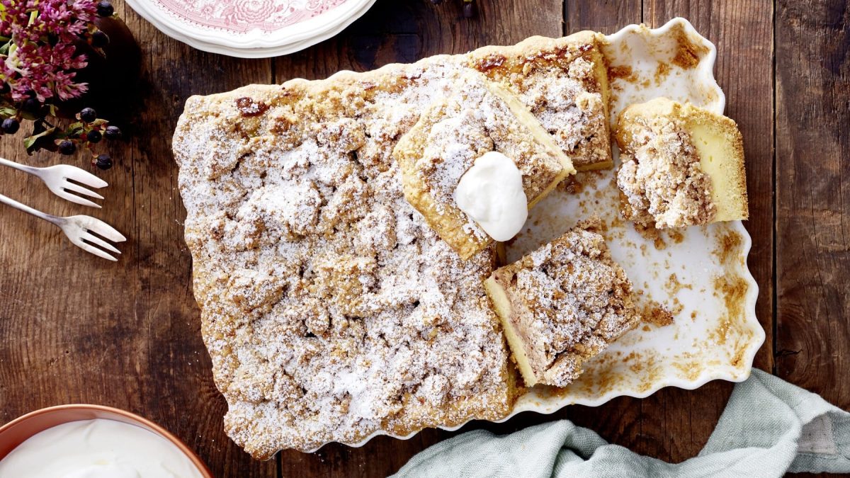 Streusel-Pudding-Tarte in einer weißen Form auf hölzernem Tisch, bestreut mit Puderzucker.