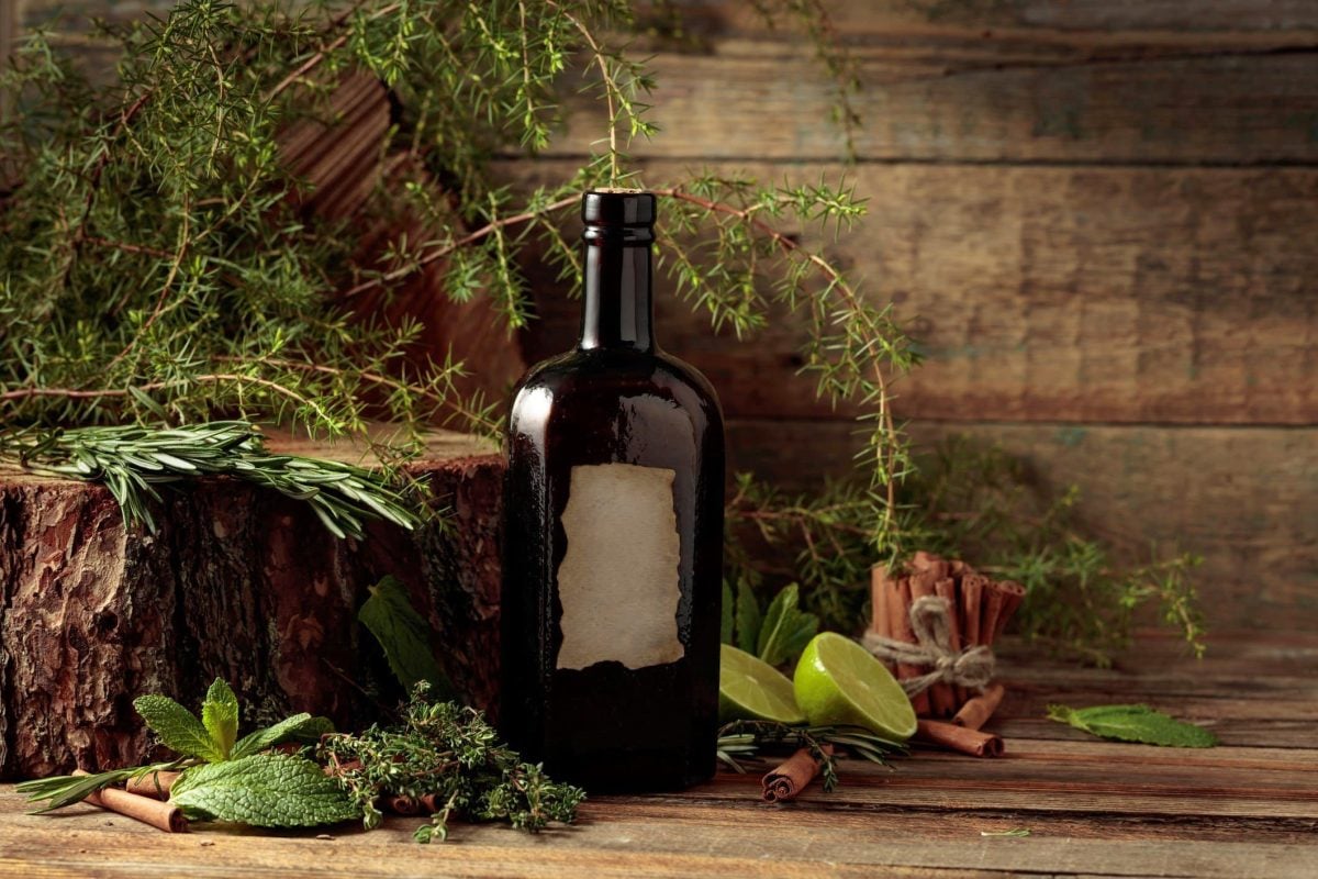 Was ist Gin und was sind Botanicals vintage Gin-Flasche und Botanicals auf Holztisch. Daneben Holzklotz mit Kräutern. Frontalaufnahme.