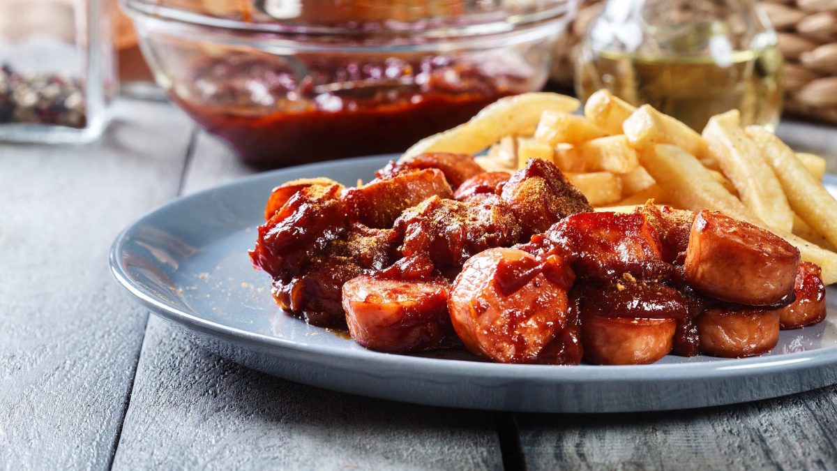 Ein Teller vegane Currywurst mit Sauce und Pommes.