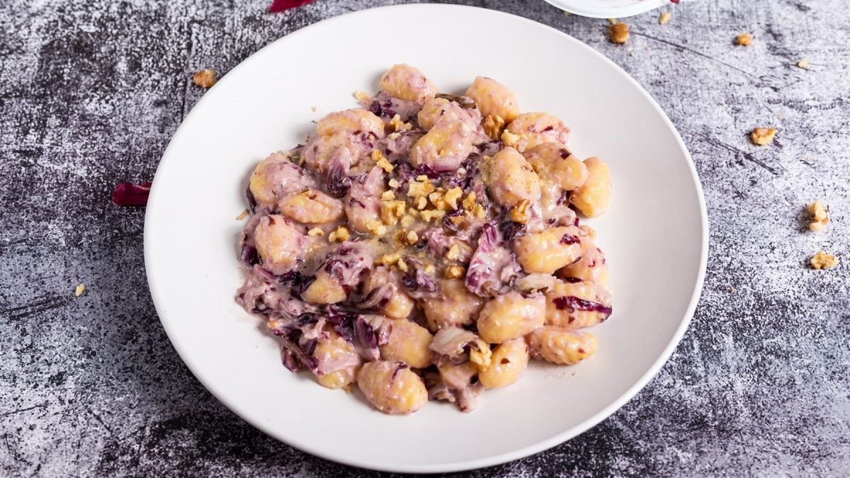 Ein Teller vegane Gnocchi mit Radicchio und Walnüssen auf schwarz-grauem Untergrund.