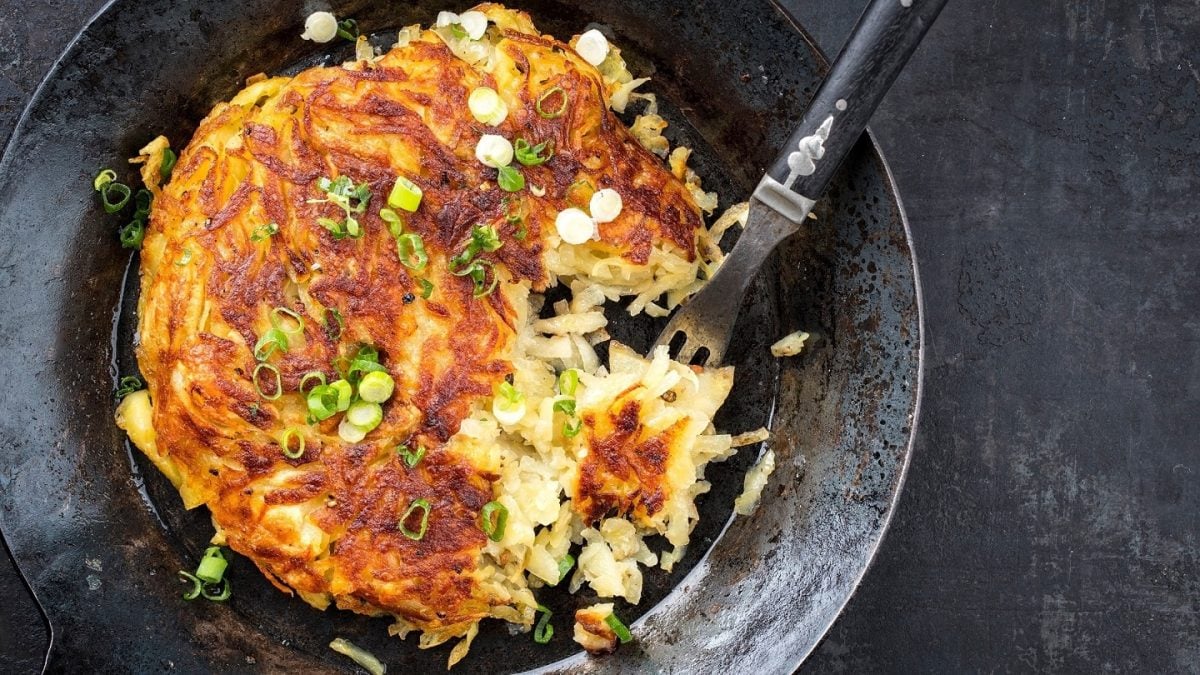Eine gusseiserne Pfanne in der Draufsicht, darin ein veganer Kartoffelpuffer mit Lauch