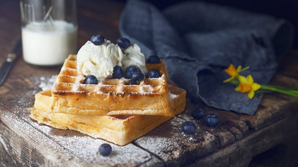 Zwei vegane Waffeln mit Blaubeeren und einer Kugel Vanilleeis auf rustikalem Holz.