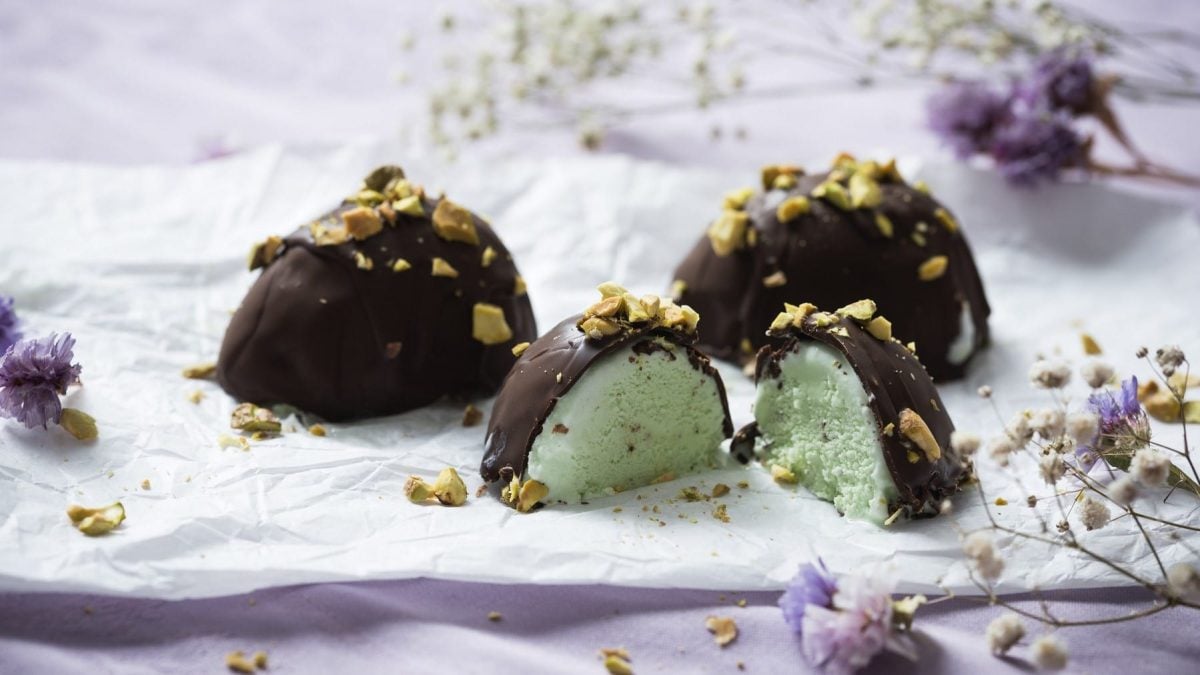 Selbst gemachtes veganes Eiskonfekt mit Pistazienfüllung, bestreut mit frischem Pistazienhack und serviert auf einem hellen Tuch.