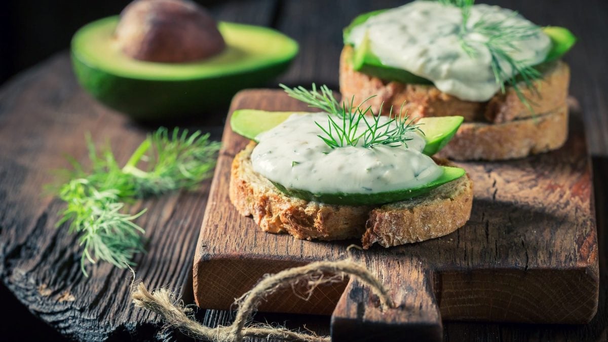 Baguettescheiben mit veganem Tzatziki mit Avocado auf einem rustikalen Holzbrett.