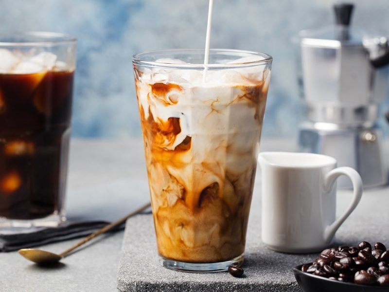 Vietnamesischer Eiskaffee in einem Glas mit Eiswürfeln und Kaffeebohnen auf einem hellgrauen Tisch