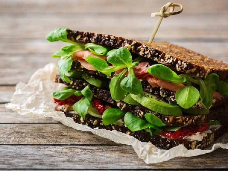 Auf einem Tisch liegt ein Vollkornbrot mit Schinken, Salat und Avocado.