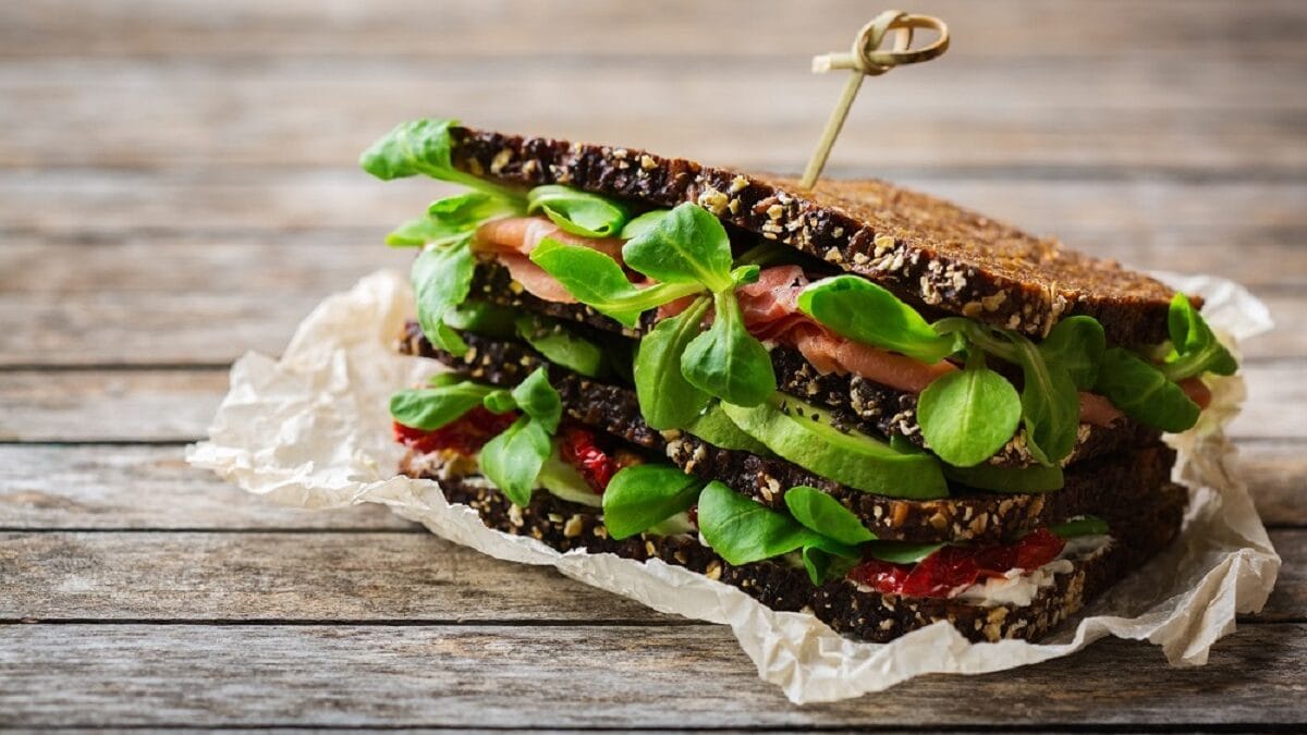 Auf einem Tisch liegt ein Vollkornbrot mit Schinken, Salat und Avocado.