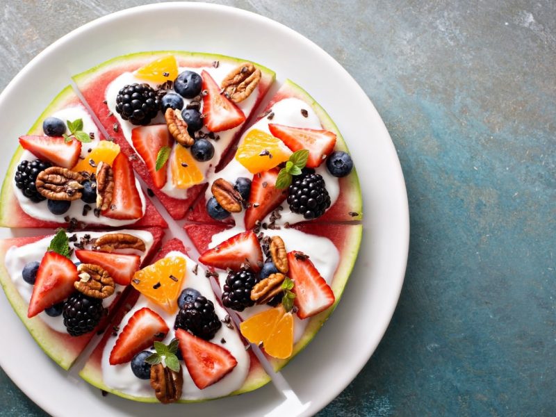 Draufsicht auf einen weißen Teller mit Wassermelonenpizza auf einem blau-grauem Untergrund
