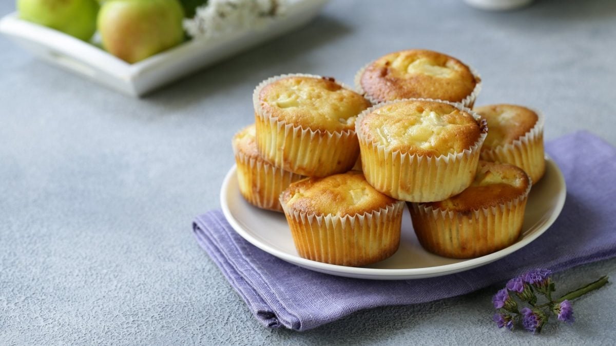 Mehrere Apfel-Muffins drapiert auf einem Teller. Angerichtet auf einem hellblauen Untergrund.