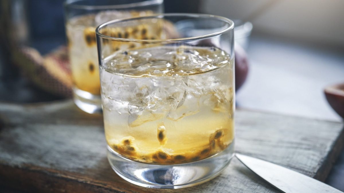 Caipirinha mit Passionsfrucht auf einem hölzernen Brett. Daneben ein Messer.