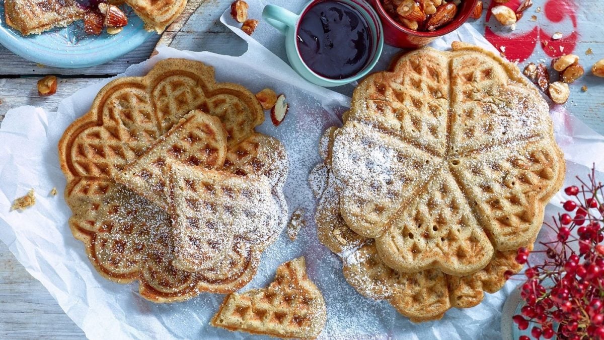 Auf einem Tisch liegen mehrere Herzwaffeln. Sie sind mit Puderzucker bestreut.