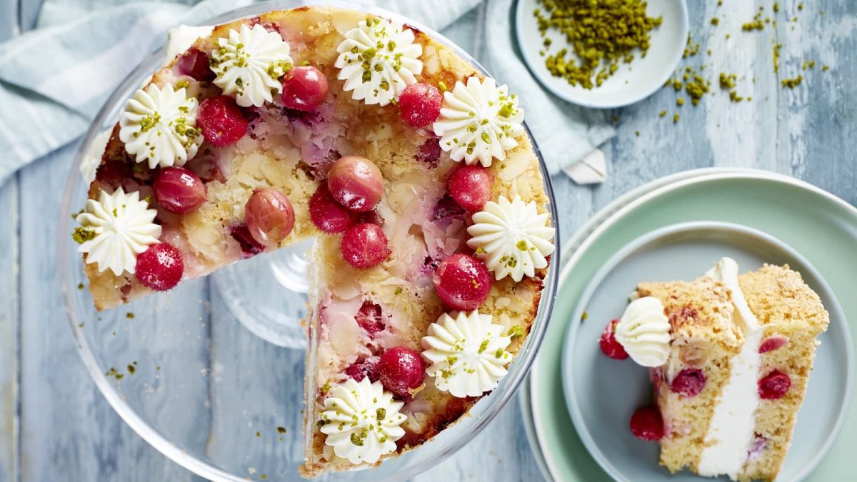 Auf einem Tisch steht eine Stachelbeer-Torte. Sie ist mit frischen Stachelbeeren und Mandelblättchen dekoriert. Am Rand wurden Tuffs aus Creme aufgetragen.