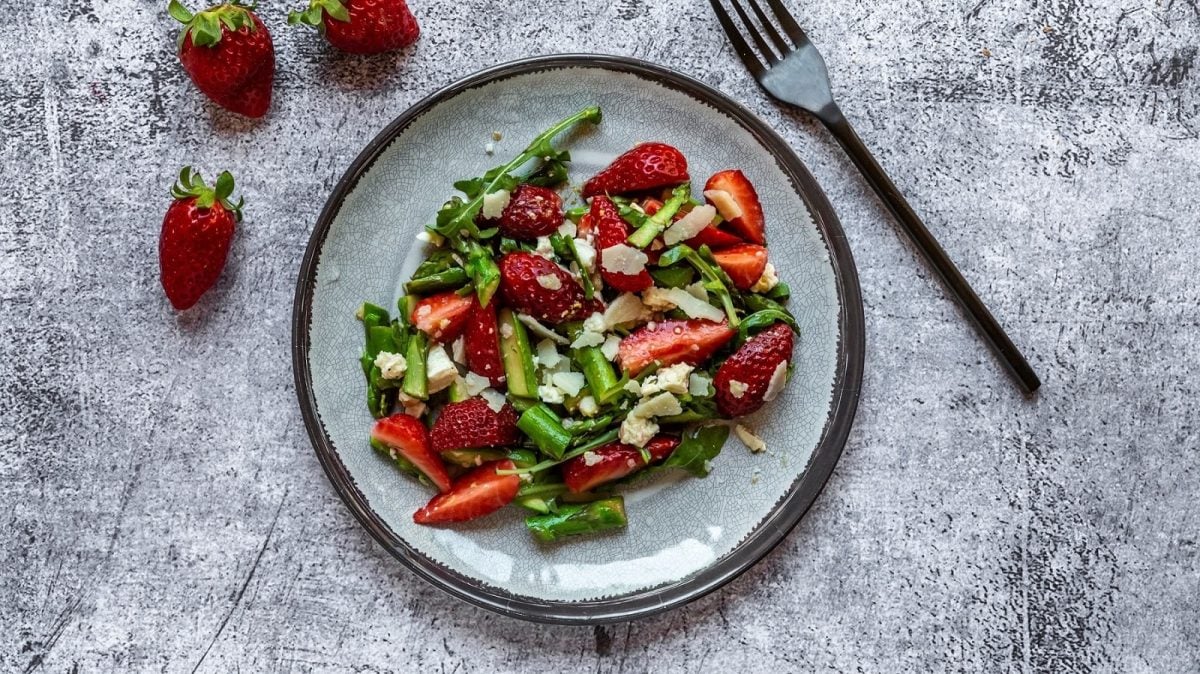 Spargelsalat mit Erdbeeren, Feta, Parmesan und Walnüssen auf hellem Teller.