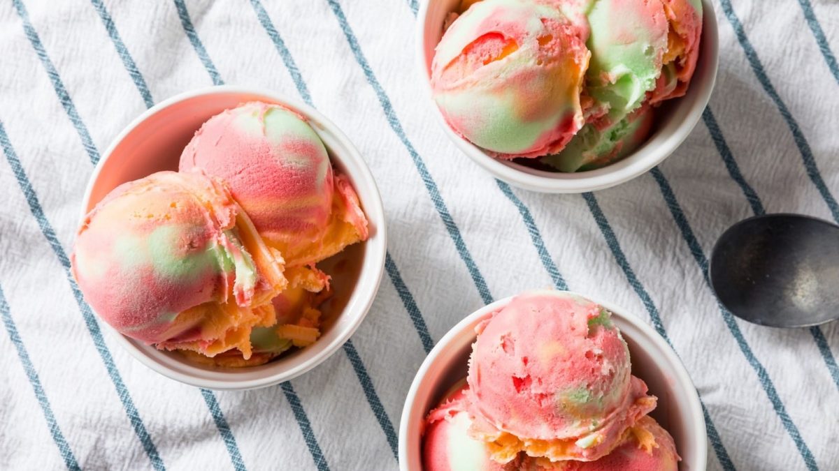 Regenbogen-Sorbet in drei Bechern auf einem gestreiften Küchentuch