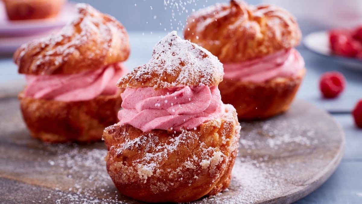 Auf einem Tablett stehen drei Himbeer-Sahne-Muffins. Sie sind mit Puderzucker bestreut und mit Creme gefüllt.