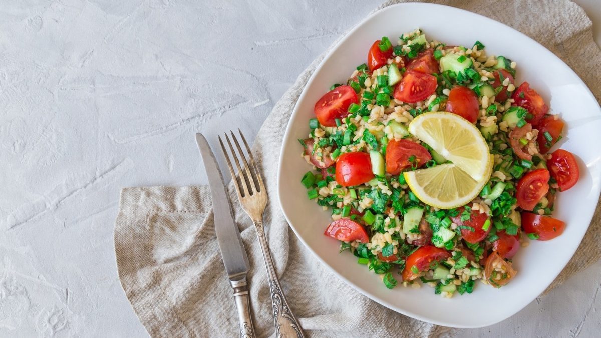 Auf einem teller ist ein schneller Bulgursalat mit Tomaten und Zitrone angerichtet.