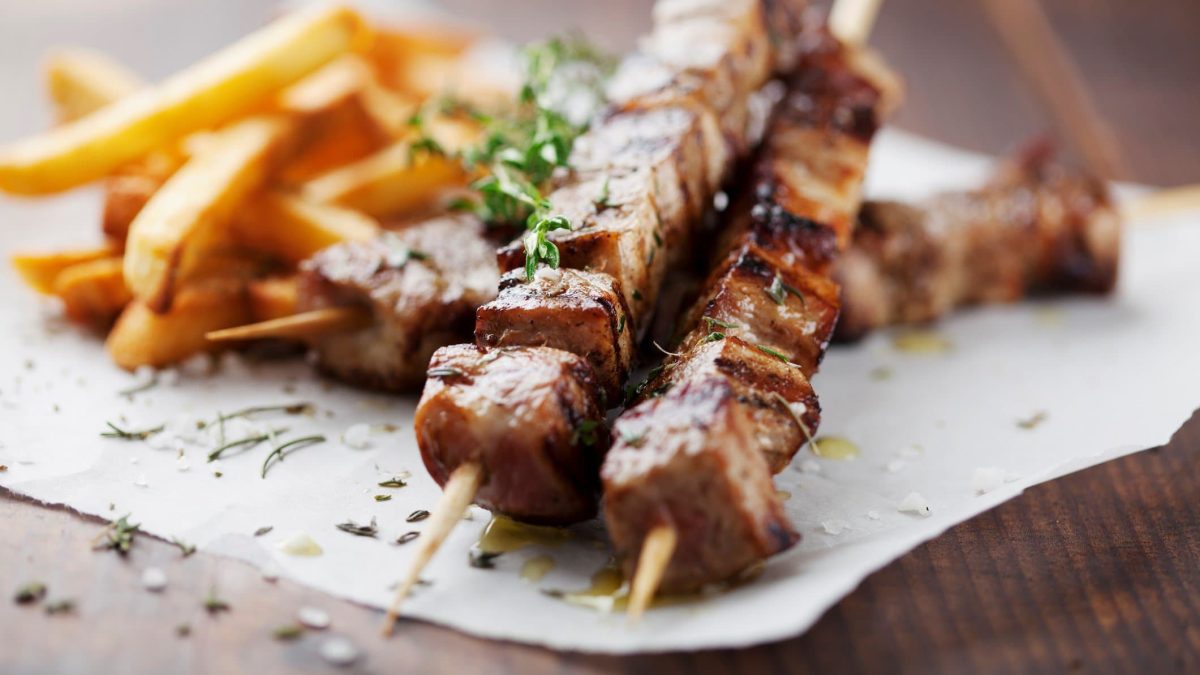 Souvlaki-Spieße mit Pommes frites auf Papier, angerichtet auf Holzuntergrund.