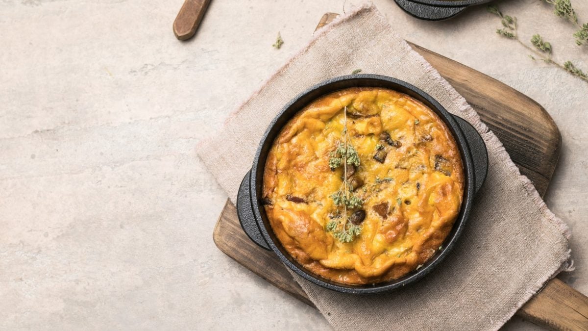 Gusseiserne Pfanne mit Speck-Pilz-Frittata auf hellem Untergrund.