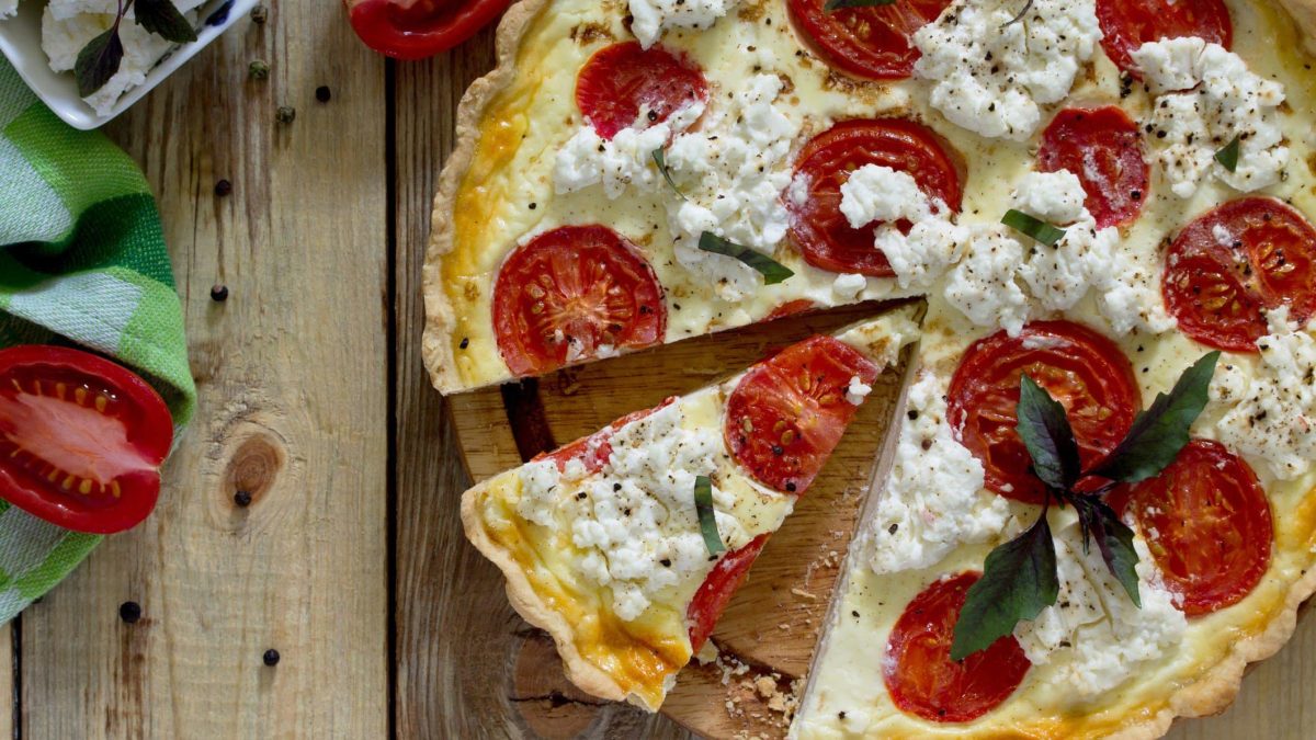 Tomaten-Ricotta-Quiche mit frischem Pfeffer auf hölzernem Untergrund.