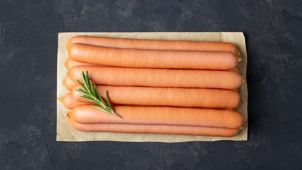 Wiener Würstchen einfrieren: Eine Portion Wiener Würstchen werden dafür auf einem Backpapier ausgelegt dafür vorbereitet. Sie liegen auf einem Papier auf einem Schiefertisch und sind mit einem Rosmarin-Zweig garniert