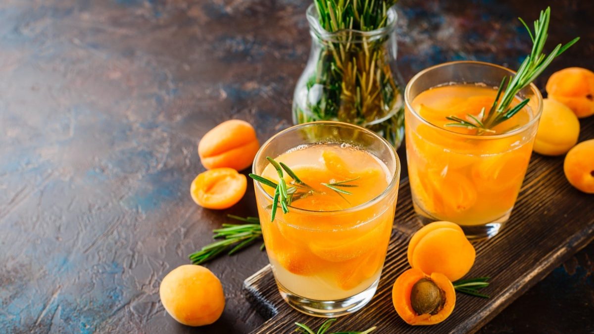Aprikosen-Cocktail mit Rosmarin und kleinen Aprikosen in zwei Gläsern, garniert mit frischem Rosmarin und serviert auf einem dunklen Steintisch.