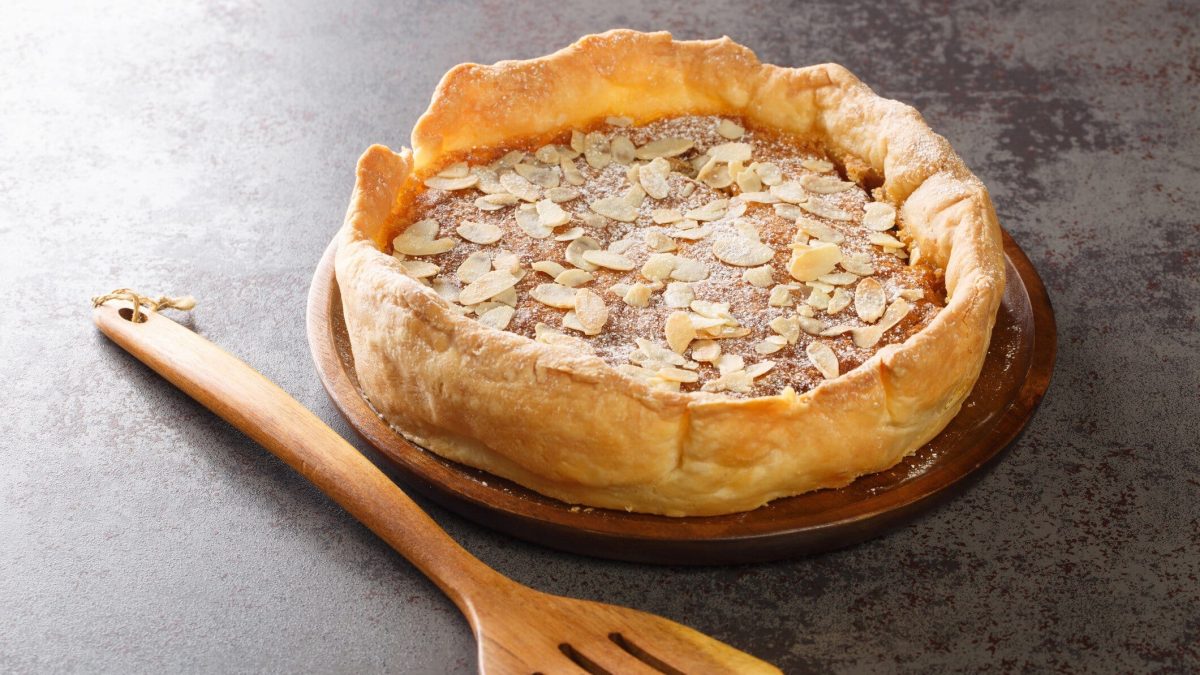 Ein Bakewell Pudding auf grauem Untergrund mit einem Holzkochlöffel.