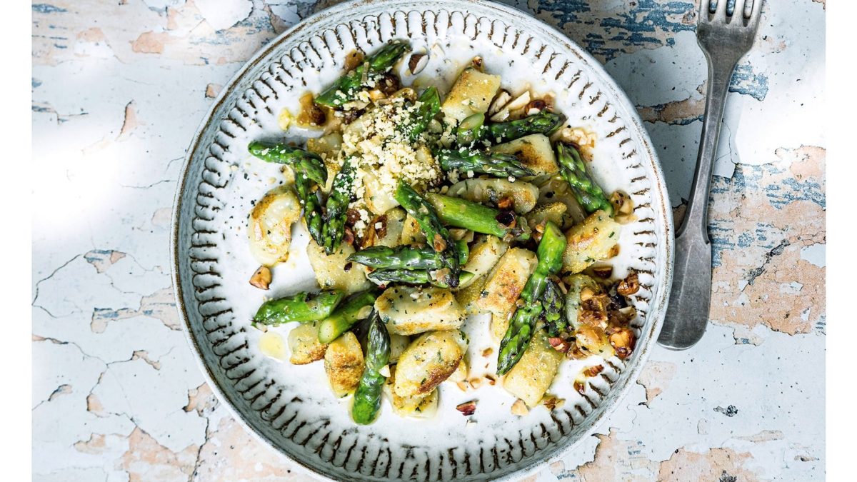 Ein Teller Basilikum-Gnocchi mit gebratenem grünem Spargel auf rustikalem Untergrund in der Draufsicht.