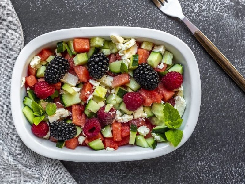 Eine Schüssel mit einem Beerensalat mit Melone und steht auf einem dunklen Hintergrund.