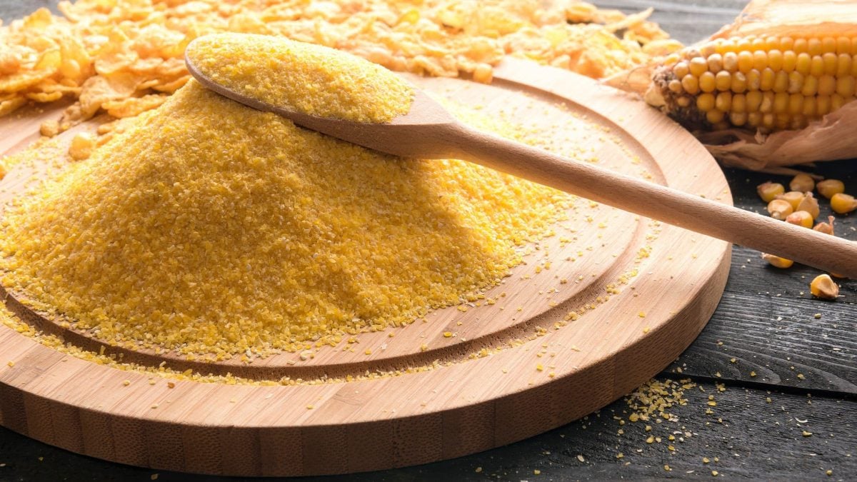 Maismehl auf einem Schneidebrett mit einem Holzlöffel und Cornflakes auf schwarzem Untergrund.