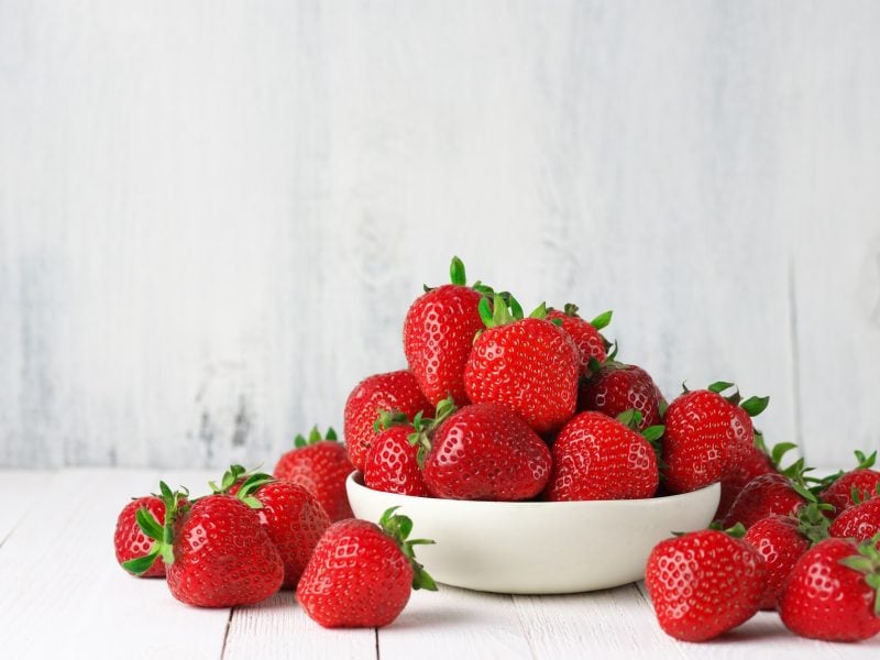 Eine weiße Schlale mit ERdbeeren. Drum herum liegen auch Erdbeeren.