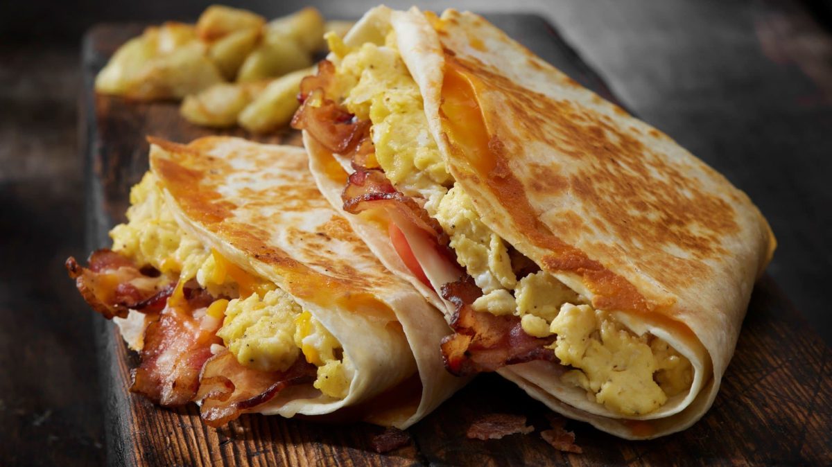 Frühstücks-Tortilla auf schwarzem Tisch mit Rührei und Speck.