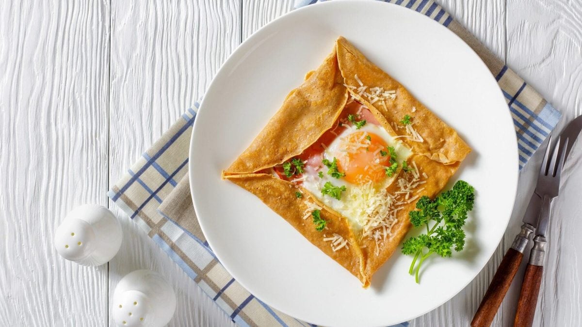 Auf einem weißen Teller liegt ein Buchweizen-Buchweizen-Pfannkuchen mit Schinken, Ei und Käse