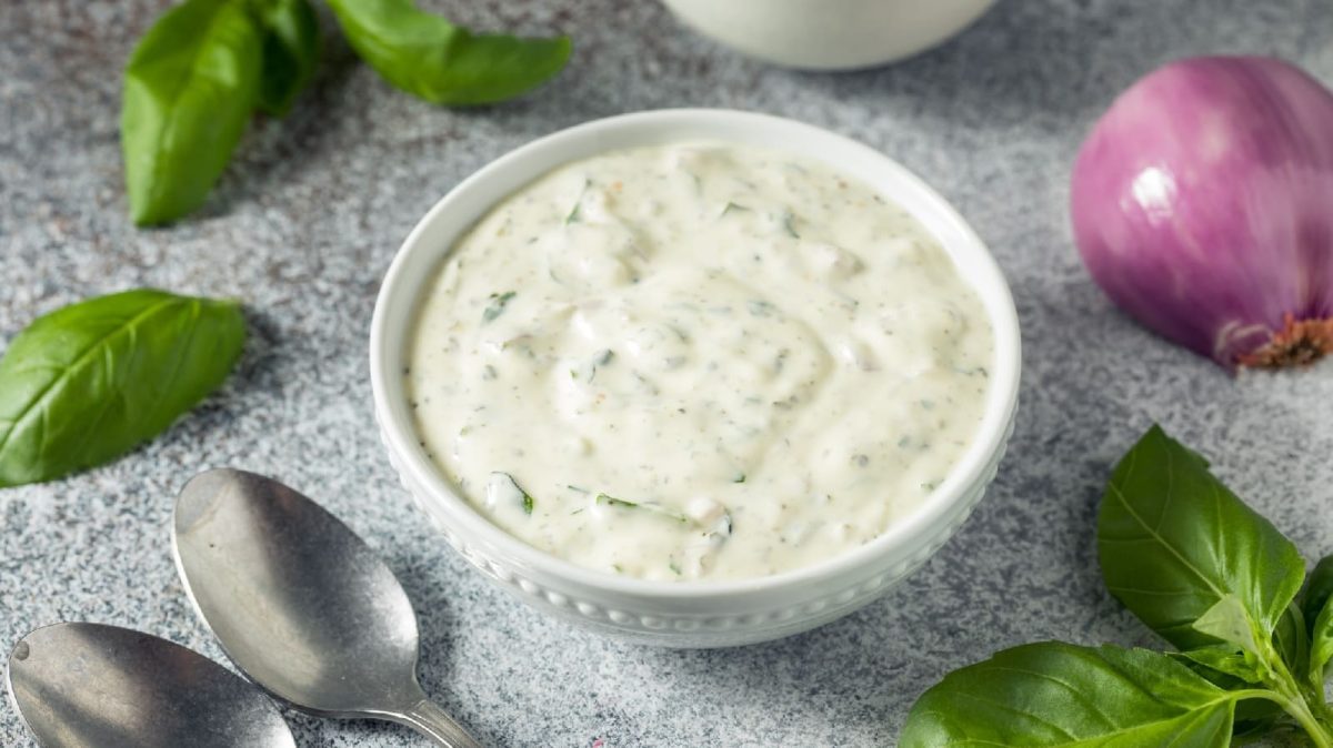 Green Goddess Dip vin einem weißen Gefäß neben zwei Löffeln und Basilikumblättern