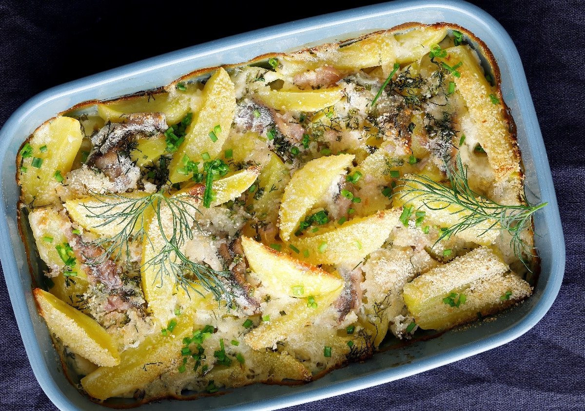 Eine Auflaufform mit Kartoffel-Anchovi-Auflauf auf einem dunklen blauen Tuch.