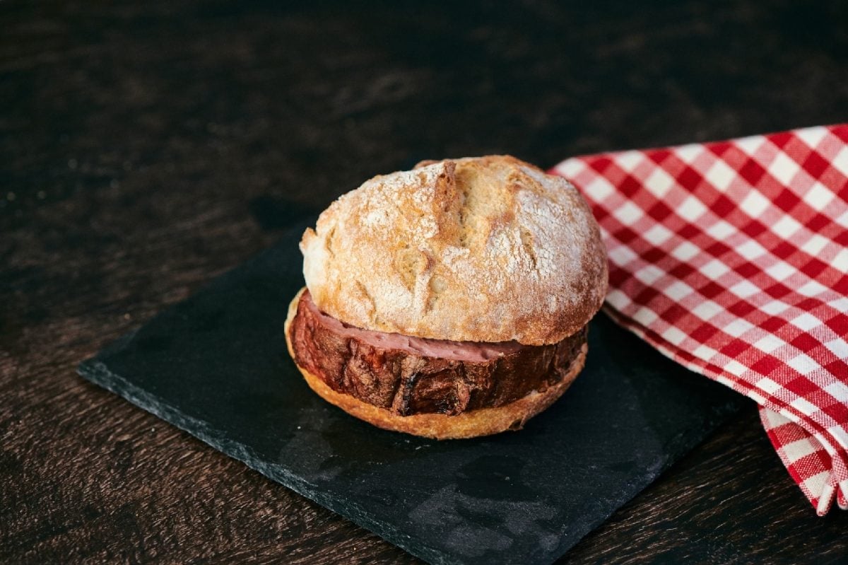 Brötchen mit Leberkäse innen auf einer Schieferplatte neben einem rot karierten Tuch