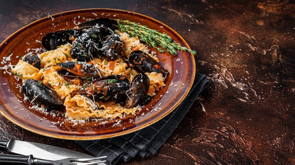 Mafaldine mit Miesmuscheln an einer Tomatensauce auf einem braunen- Teller und einem dunkelbraunem Holztisch.