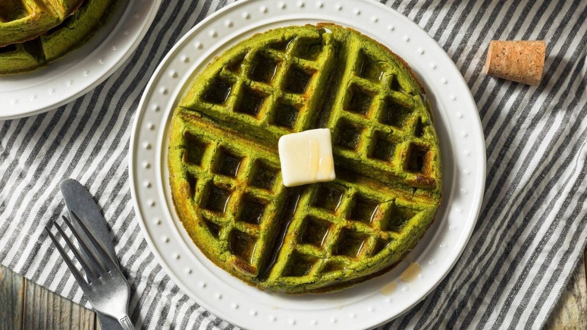 Pandan-Waffeln mit einem Stück Butter auf einem weißen Teller, der auf einem blau-weiß gestreiften Geschirrtuch liegt