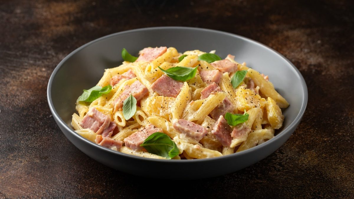 Eine graue Schale mit der Pasta Hawaii auf einem dunklem Holztisch.