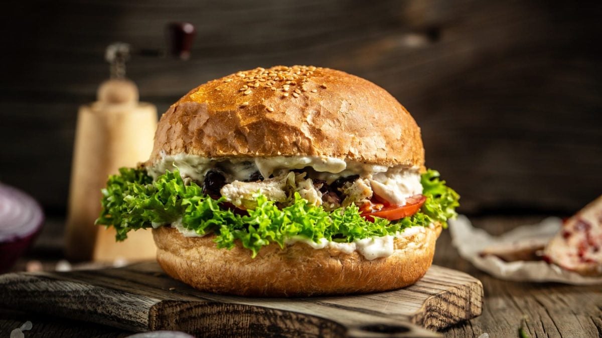 Pulled Chicken Burger auf einem Holzbrett. Im Hintergrund verschiedene Zutaten.