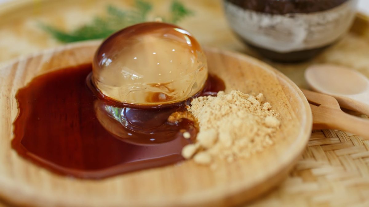 Aloe Vera Raindrop Cake mit Kokosblütensirup und geröstetem Sojamehl auf einer runden Holzplatte