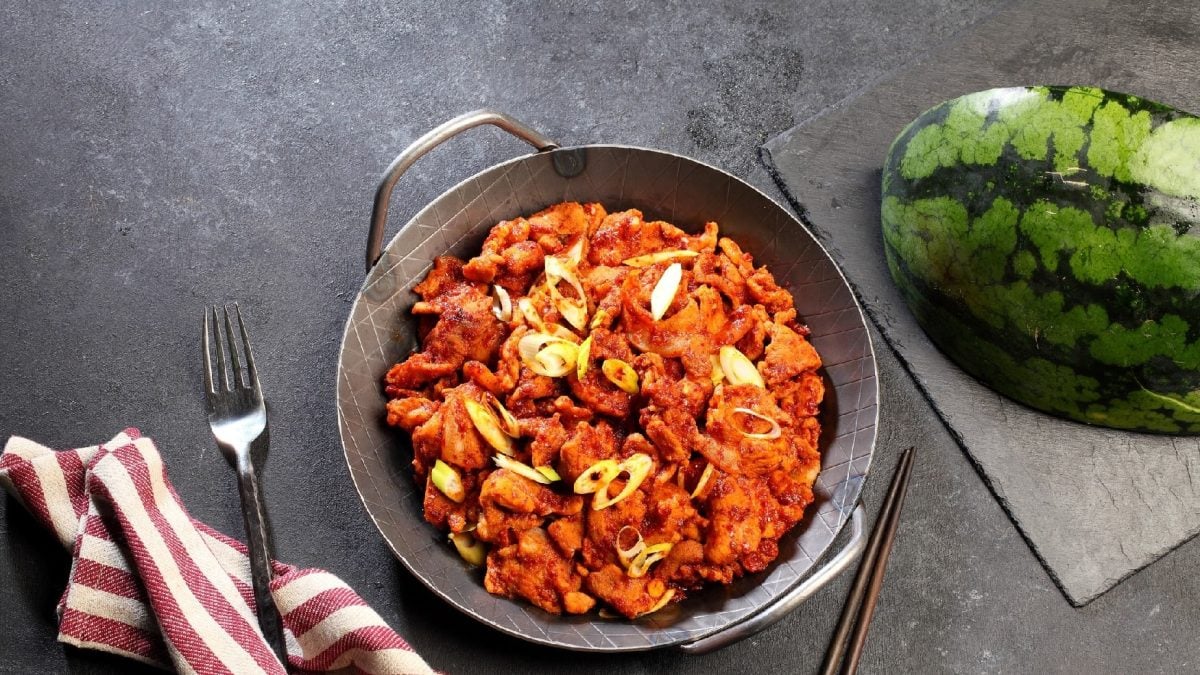 Eine gusseiserne Pfanne mit dem Rindfleisch-Melonen-Ragout auf dunklem Untergrund. Unten links im Bild ein Tuch und oben rechts im Bild eine Wassermelonenspalte.