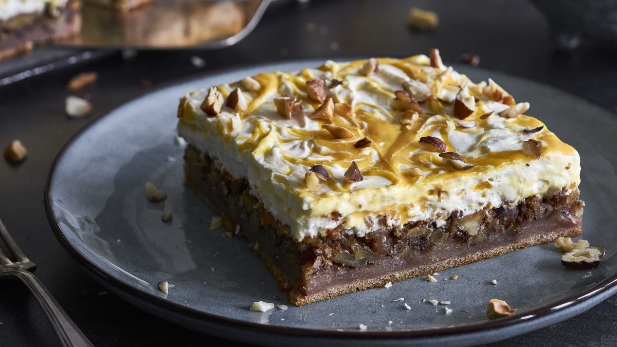 Schmandkuchen mit Karamellsauce auf einem grauen Teller. Daneben liegt eine Gabel.