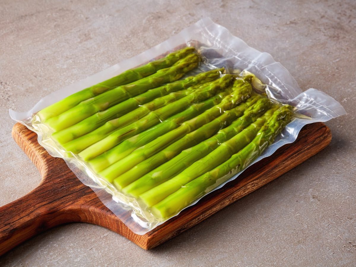 Vakuumierter Spargel auf einem Holzbrett und Steinuntergrund.