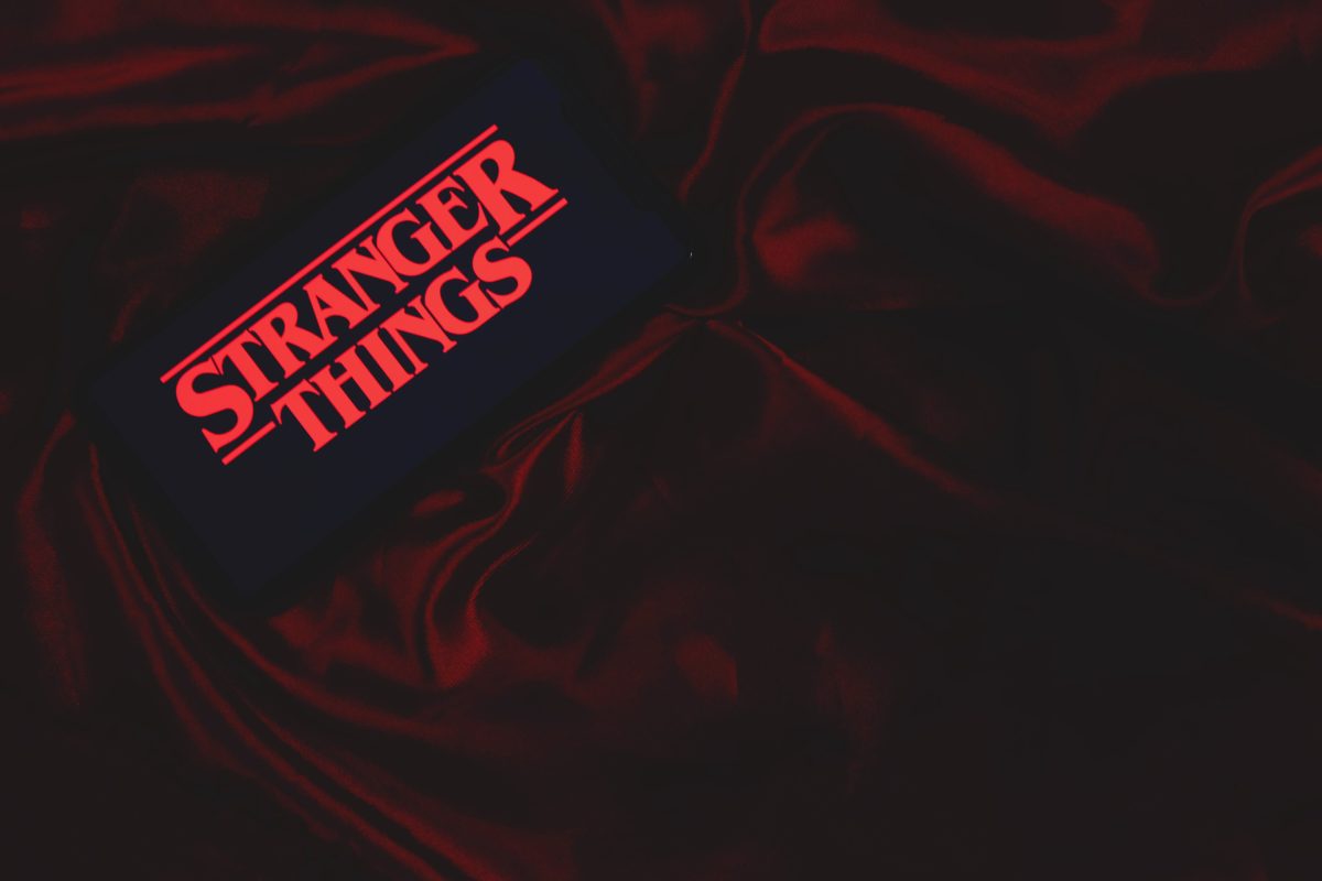 80er Jahre Retro-Menü zur vierten Staffel Stranger Things roter Schriftzug auf Mobiltelefon auf roter Samtdecke. Aufnahme aus der Vogelperspektive.