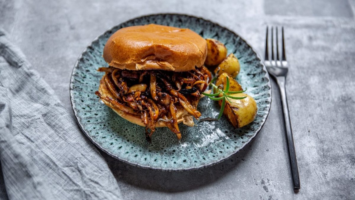 Veganes Pulled Pork aus Austernpilzen in einem Burger serviert auf einem blauen Teller.