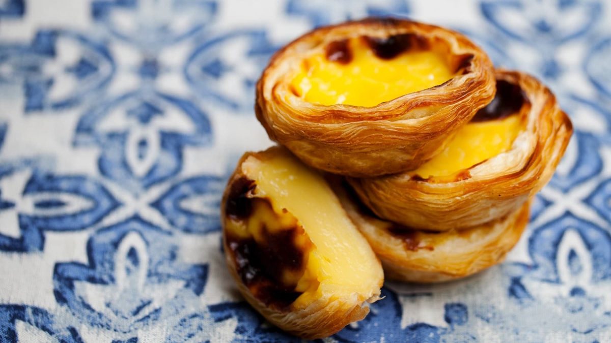 ein Stapel veganer Pasteis de Nata auf blau-weißen Fliesen.