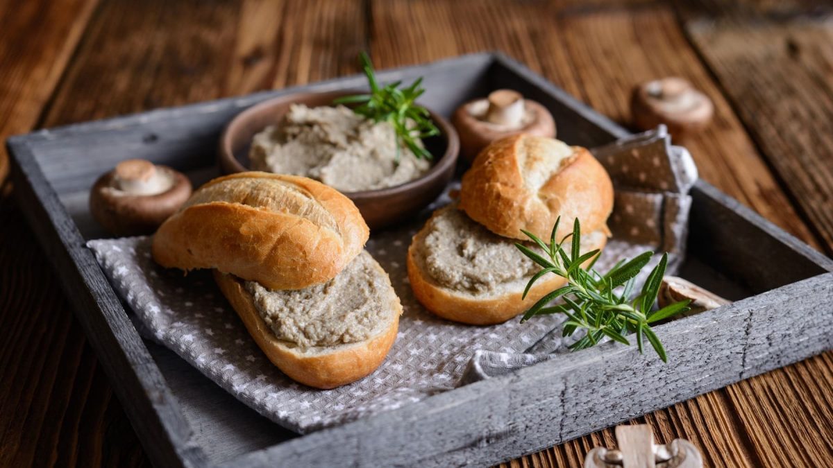 Zwei Brötchen mit veganem Brotaufstrich mit Chamoignons auf einem Tablett, außerdem eine Schale mit dem Brotaufstrich und frische Pilze.